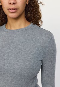 Šedé tričko s dlouhým rukávem a kulatým výstřihem. Vyrobené z měkké, texturované látky. Má přiléhavý střih a viditelné prošití na švech.