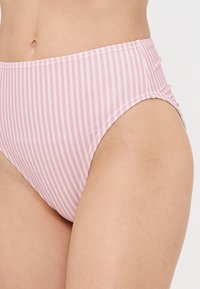 Costum de baie cu talie înaltă, de culoare roz, cu dungi verticale albe, fabricat dintr-un material neted cu o ușoară strălucire și detalii cu bandă elastică la talie.