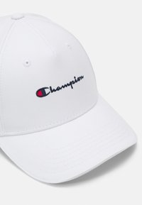 Biely baseballový klobúk vyrobený z bavlneného materiálu s vyšívaným logom "Champion" v námorníckej a červenej farbe na prednej strane. Štruktúrovaný dizajn s zakriveným okrajom.