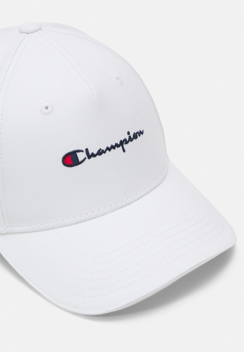 Gorra de béisbol blanca hecha de material de algodón con un logotipo bordado "Champion" en navy y rojo en la parte frontal. Diseño estructurado con visera curvada.