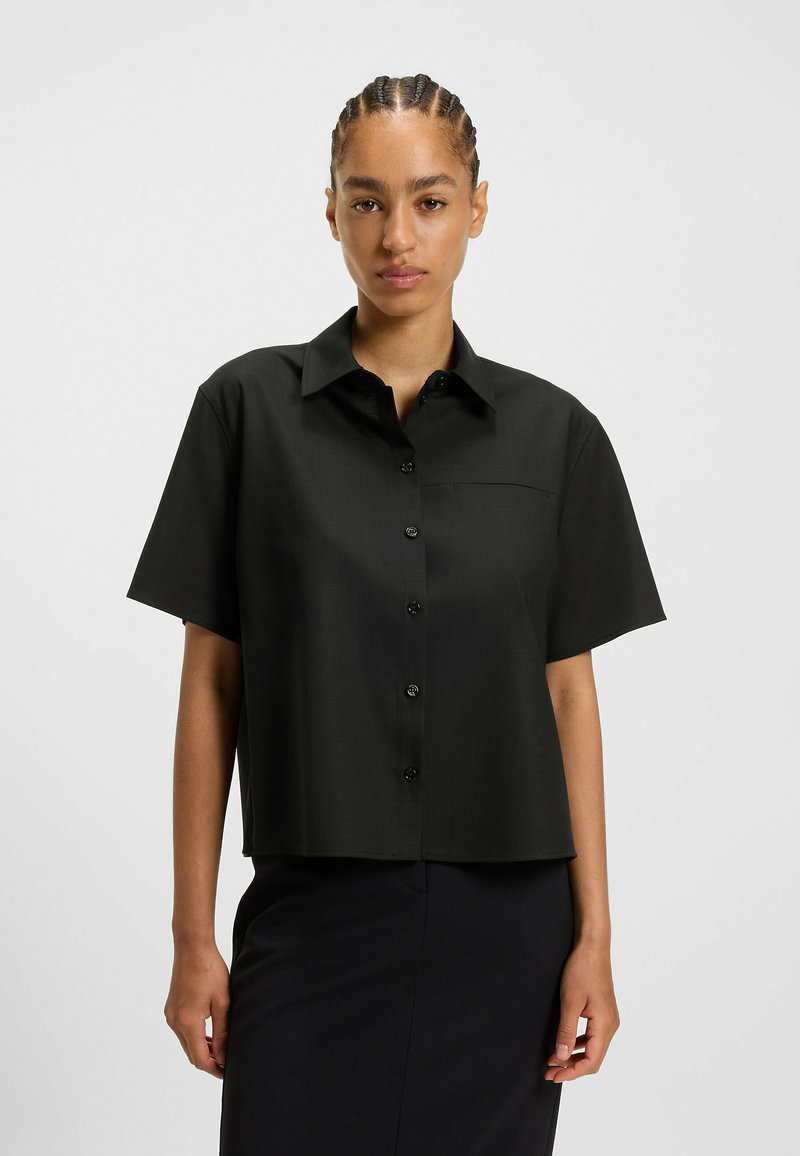 Black short-sleeve shirt with a button front, collar, and chest pocket. Smooth texture with a relaxed fit and straight hem.