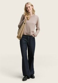 Pull beige clair à col rond côtelé, associé à un jean large bleu foncé et des chaussures à plateforme noires ; tenant un sac beige.