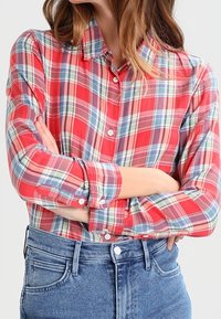 Camisa a cuadros roja y azul con cuello, mangas largas arremangadas en los puños y un par de pantalones vaqueros de talle alto.