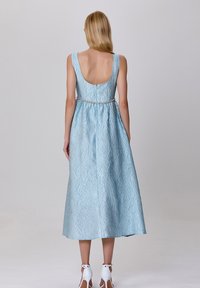 Robe sans manches bleu clair avec un tissu texturé, un dos décolleté et une taille ajustée soulignée par une fine ceinture décorative.
