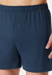 Boxers bleu marine en tissu doux, avec un motif géométrique et une taille élastique avec une fermeture à bouton fonctionnelle.