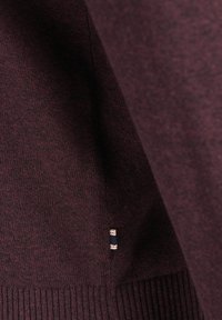 Suéter burdeos con una textura suave, que presenta un dobladillo acanalado y un pequeño acento de marca en el lateral.
