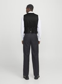 Black vest with a smooth texture and peplum design at the back, paired with plain black trousers and black shoes. White shirt underneath.