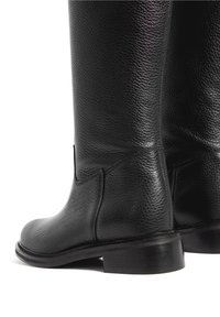 Bottes en cuir noir montantes jusqu'aux genoux avec une finition texturée, bout arrondi et talon bas et robuste. Présentent des accents de couture subtils.