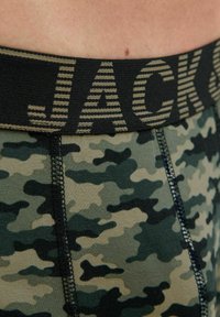 Grüne Tarnbriefs mit einem schwarzen elastischen Bund, der "JACK" in gestreichem Text zeigt. Glatte Stofftextur mit kontrastierenden Nähten.