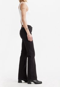 Zwarte flared jeans van denim, met een hoge taille, subtiele stikdetails en een leren label op de achterband.