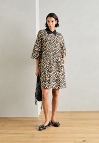 Haljina s uzorkom leoparda, crnim ovratnikom, kratkim rukavima, dva prednja džepa i ležernim krojem, uparena s crnim balerinkama i malom torbicom.
