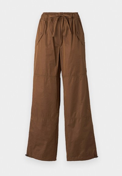 Wide-leg brown pants made of lightweight fabric, featuring an elastic waistband, drawstring, side pockets, and bottom zipper details.