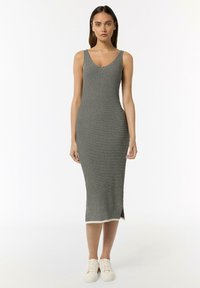 Gestreiftes, ärmelloses Kleid in knielanger Schwarz-Weiß-Baumwollmischung, mit Rundhalsausschnitt und seitlichen Schlitzen, kombiniert mit weißen Turnschuhen.