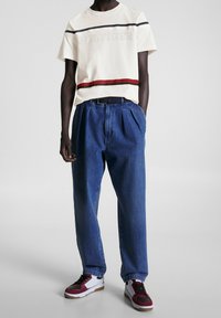 Camiseta blanca de manga corta con rayas rojas y azul marino, combinada con jeans azules de cintura alta y pliegues, y zapatillas negras, rojas y blancas.