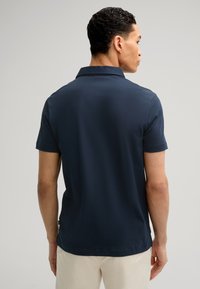 Polo de manga corta azul marino con cuello clásico y tejido texturizado. La vista trasera revela un diseño limpio y un ajuste ligeramente entallado.
