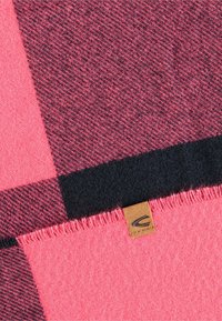 Wolldecke mit einem Karomuster in Rosa, Burgunderrot und Schwarz, veredelt mit fransigen Kanten und einem kleinen braunen Lederetikett.