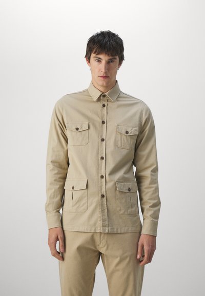 Beige, button-up shirt made of cotton with two chest pockets, a collared neckline, and long sleeves. Features brown buttons and a straight fit.