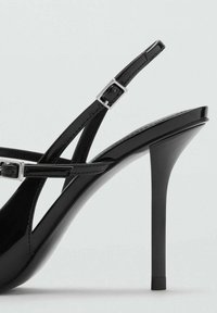 Sandales noires à talons hauts avec une finition laquée brillante, des sangles ajustables fines, un matériel en argent et un design à bout pointu.