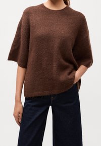 Pull marron tricoté à manches courtes, texture douce, coupe large et décontractée. Associé à un pantalon en denim foncé avec une jambe droite.