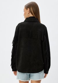 Zwarte suède jas met franjes langs de mouwen en op de rug, met een kraag en knoopmanchetten. Gecombineerd met denim shorts.