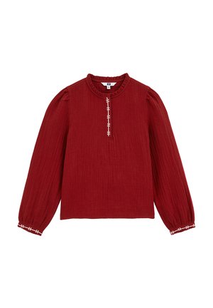 Blouse rouge à manches longues en tissu texturé avec un col rond à volants, présentant des coutures décoratives blanches le long de la patte de boutonnage et des poignets.