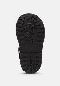 Suela de zapato de goma negra con un patrón de textura en la suela, presentando una marca en relieve y el número "18" exhibido de manera prominente.