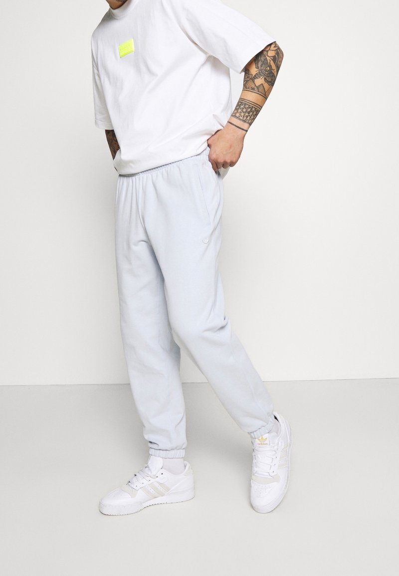 Světle modré tepláky s elastickým pasem, bočními kapsami a žebrovanými manžetami, doplněné bílým tričkem a bílými teniskami.