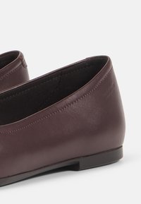 Ballerines en cuir bourgogne avec une texture lisse, bout rond et talon bas. Doublure intérieure noire avec un léger éclat. Design minimaliste.