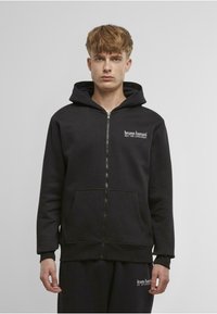 Black zip-up hoodie made of cotton blend, featuring a front pocket, adjustable drawstring hood, and white logo text on the chest.