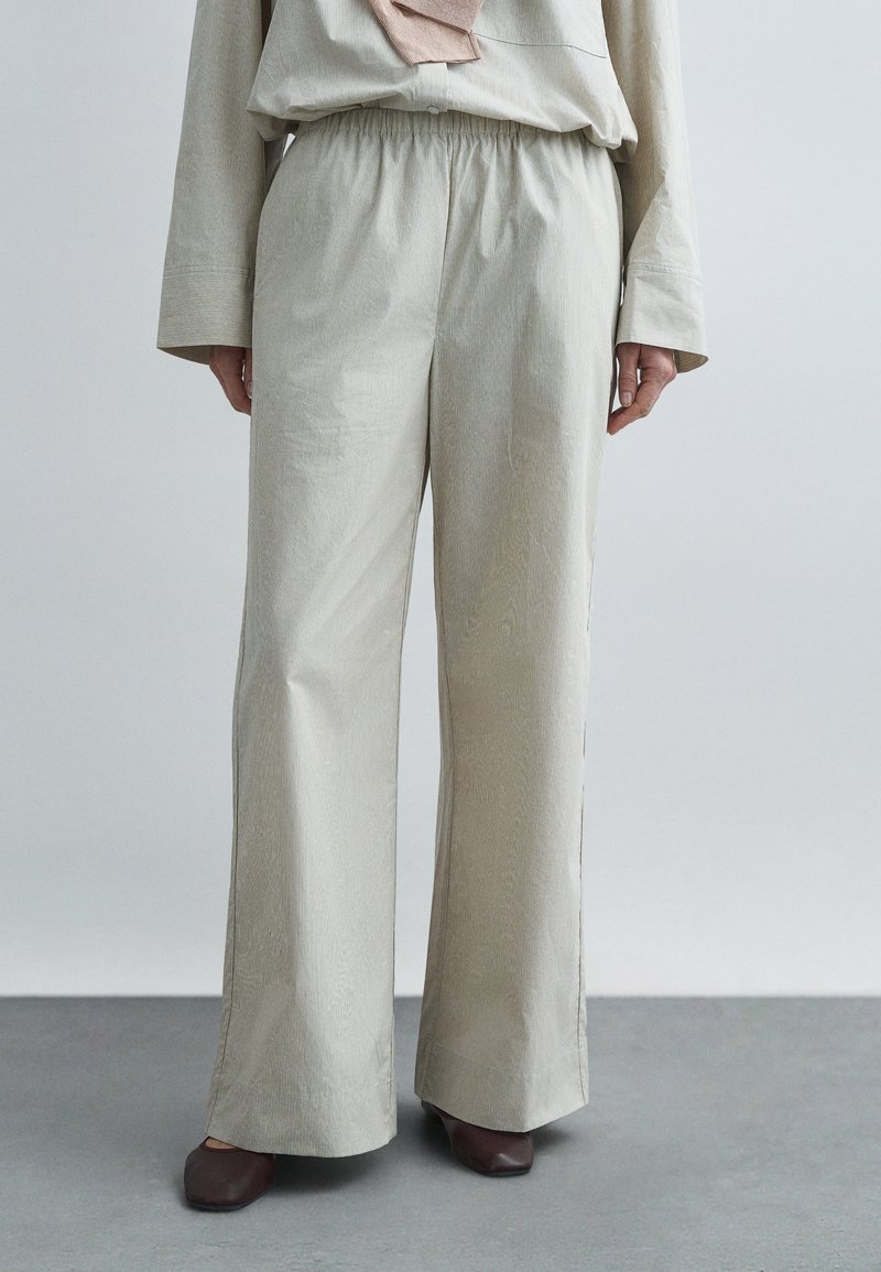 Pantalon ample beige clair avec un motif texturé, taille élastique et jambes droites, associé à des chaussures marron sans lacets.
