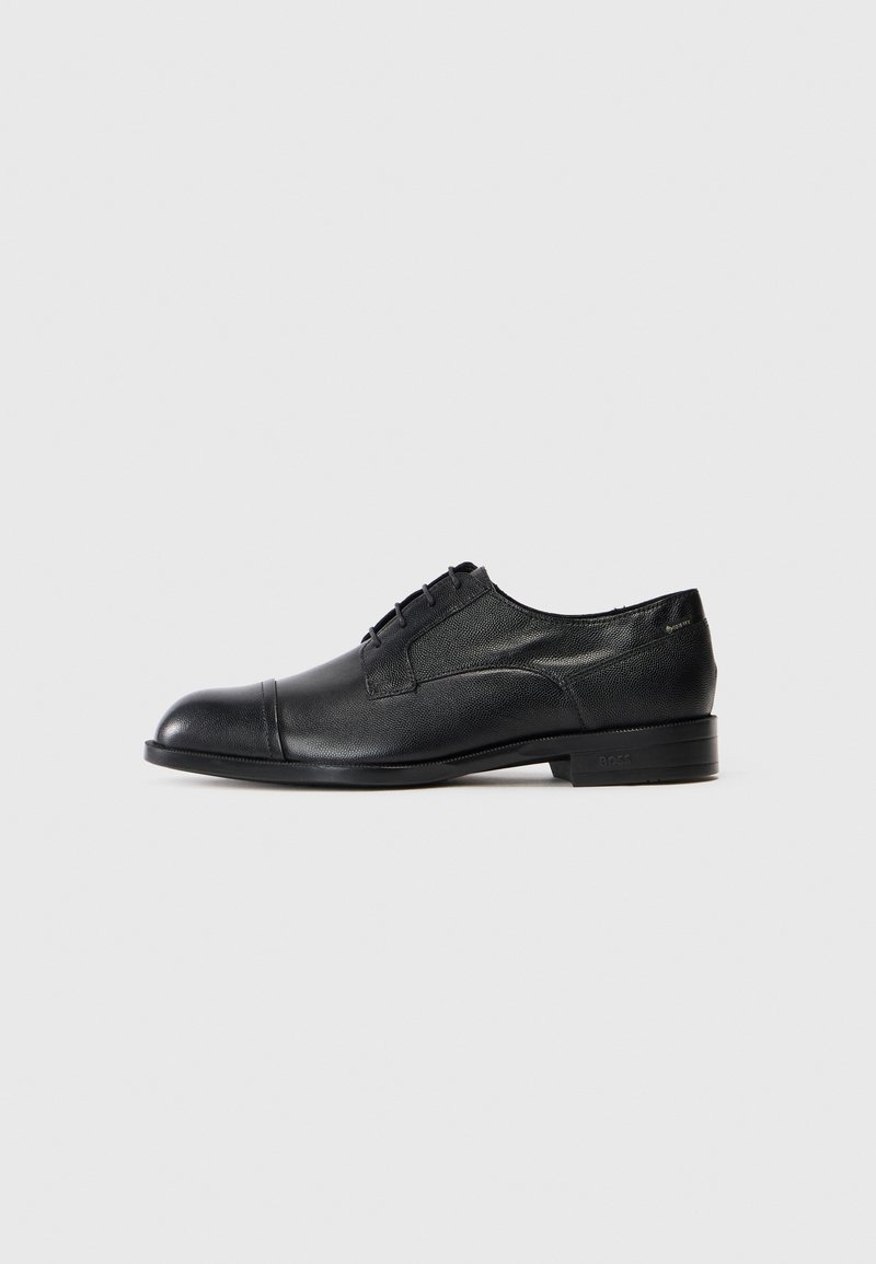 Zwarte leren nette schoen voor heren met een cap toe, vetersluiting en een lage hak op een effen lichte achtergrond.