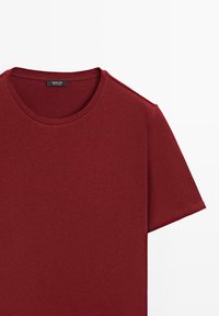 T-shirt à manches courtes et col rond en rouge profond uni avec une étiquette de col visible sur un fond blanc uni.