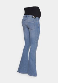 Jeans flare de maternidade em denim azul claro. Apresenta uma cintura preta sobre a barriga, bolsos traseiros e um acabamento ligeiramente desbotado.