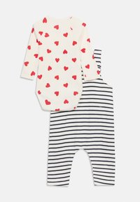 Λευκό βρεφικό φορμάκι με μακριά μανίκια και κόκκινη καρδιά, και λευκό φορμάκι χωρίς μανίκια με οριζόντιες μπλε σκούρες ρίγες.