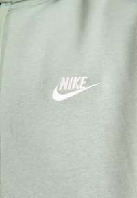 Hoodie verde-claro feito de tecido macio, apresentando um logótipo da Nike bordado em branco no peito. Textura suave, design casual.