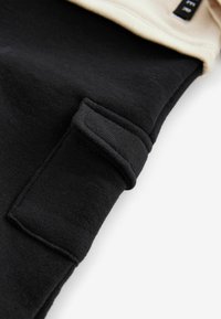Jogger de algodón negro con detalle de bolsillo, textura suave y cintura en crema en contraste. Líneas limpias y diseño casual.