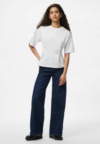 Bjela kratka majica s opuštenim krojem, s bočnim šavovima, u kombinaciji s tamnoplavim širokim trapericama i crnim platformama.