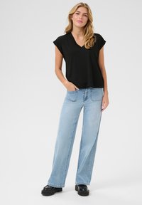 Czarny krótki top z dekoltem w serek, połączony z jasnoniebieskimi spodniami dzwonami. Model ma na sobie czarne buty na platformie. Prosty, casualowy design.
