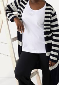 Námořnicky modrý a bílý pruhovaný cardigan přes bílý top s vyšívaným vzorem, doplněný černými kalhotami. Materiál působí měkce a pohodlně.