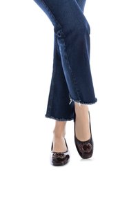 Bailarinas de charol marrón oscuro con un brillante logo doble C dorado en la puntera, combinadas con jeans de mezclilla oscura con el dobladillo desflecado.