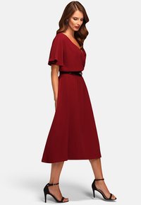 Burgundy midimekko, jossa on lyhyet liehuvat hihat, vyötärö on kireä ja siinä on musta vyö; sileä kangas; yhdistetty mustiin korkokenkiin.
