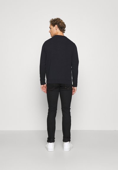 Felpa nera a maniche lunghe con scollo rotondo, abbinata a jeans neri slim-fit e scarpe da ginnastica bianche. Tessuto morbido, design semplice.