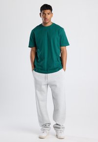 Green cotton t-shirt with a crew neckline, paired with gray sweatpants, featuring an elastic waistband and side pockets. White sneakers complete the look.