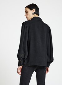 Schwarze Bluse mit einem strukturierten Kragen, Puffärmeln und Spitzenakzenten an den Manschetten. Strukturierter Stoff mit lockerem Schnitt.