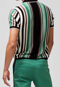 Pruhovaná polokošile s krátkým rukávem v zelené, hnědé, černé a bílé barvě, nošena s odpovídajícími zelenými kalhotami, s žebrovaným límcem a přiléhavým střihem.