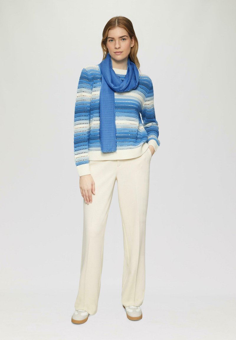 Pull en tricot rayé bleu et blanc, associé à un pantalon large couleur crème et une écharpe bleue. Modèle portant des baskets blanches.