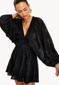 Vestido negro con mangas abullonadas y un profundo escote en V. Presenta bordados florales texturizados y una cintura fruncida. Longitud fluida, por encima de la rodilla.