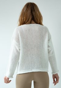 Biały sweter z dzianiny o luźnym splocie, okrągłym dekolcie i długich rękawach. Posiada lekko skrócony dół oraz ściągacze przy mankietach i u dołu.