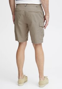Beige cargo shorts med flere lommer, rett snitt og elastisk midje. Brukt med lysebeige mockaskinnsko.
