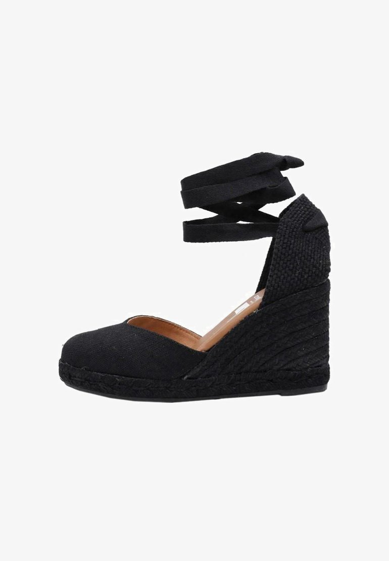 Espadrille negra de cuña con parte superior de tela, punta abierta y correas de tela entrelazadas. La textura tipo yute tejida en el talón añade un detalle.